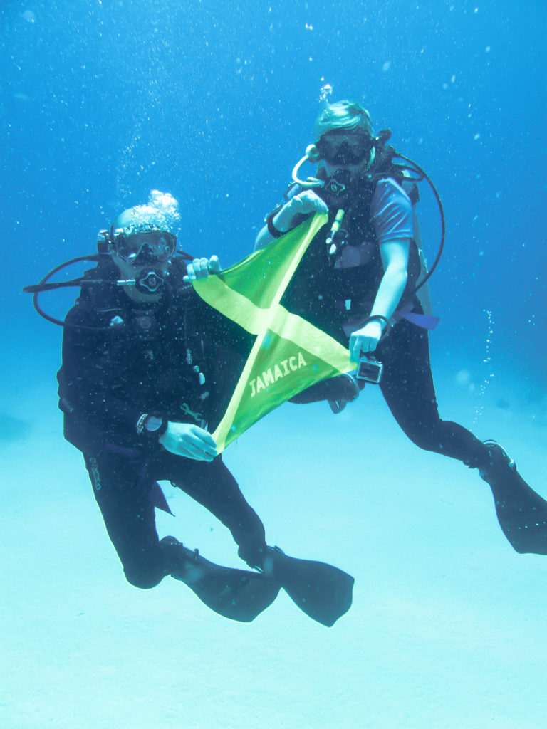 Robbie and Laura holding Jamaica flag underwater